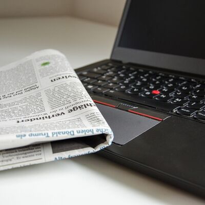 Bild vergrößern: Ein Laptop und eine zusammengefaltete Zeitung